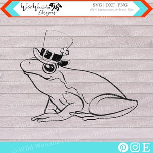 May include: Black and white line art of a frog wearing a top hat with a shamrock. The frog is sitting down. The image includes the text "Wild Wenaha Designs" and "SVG | DXF | PNG PNW Farmhouse style cut files."