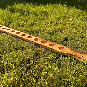 Pu&ograve; includere: Un tagliere di legno con 10 tagli circolari equidistanti. Il tagliere &egrave; di colore marrone chiaro con venature del legno naturali. Il tagliere &egrave; appoggiato su un letto di erba verde.
