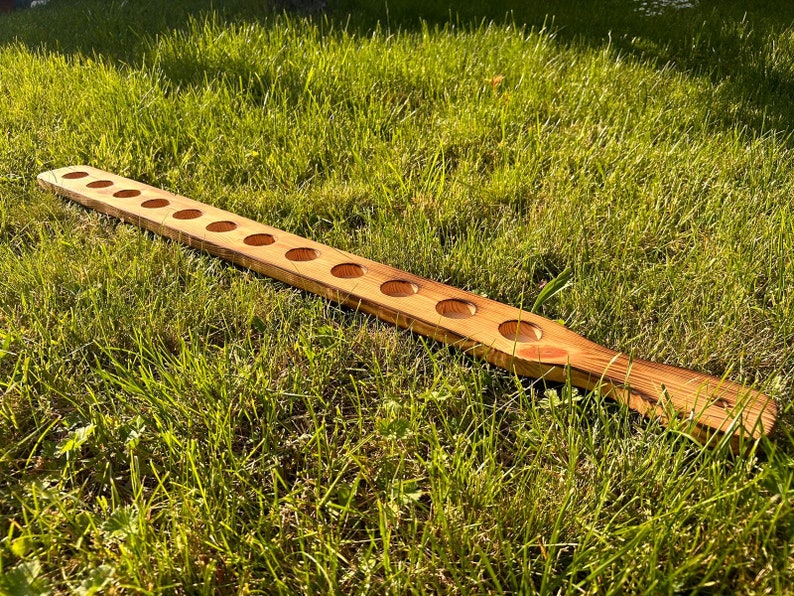 Pu&ograve; includere: Un tagliere di legno con 10 tagli circolari equidistanti. Il tagliere &egrave; di colore marrone chiaro con venature del legno naturali. Il tagliere &egrave; appoggiato su un letto di erba verde.