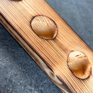 Pu&ograve; includere: Un sottobicchiere in legno con tre tagli circolari. Il sottobicchiere ha una finitura in legno naturale con un bordo bruciato marrone scuro.