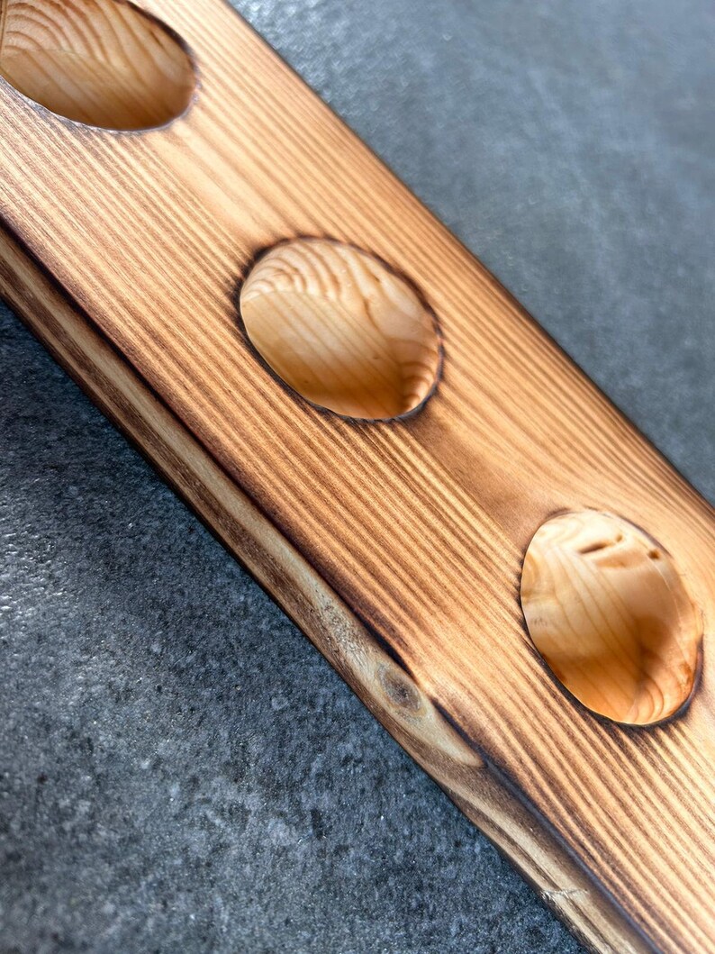 Pu&ograve; includere: Un sottobicchiere in legno con tre tagli circolari. Il sottobicchiere ha una finitura in legno naturale con un bordo bruciato marrone scuro.