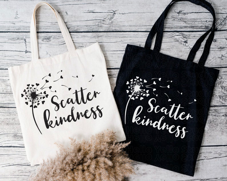 May include: Two tote bags with the text "Scatter kindness" printed on them. One bag is white with black text and a black dandelion design. The other bag is black with white text and a white dandelion design.