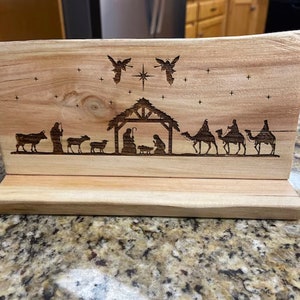 May include: A wooden Christmas nativity scene with a brown wood base. The scene features a manger with the baby Jesus, Mary, and Joseph. There are also angels, a star, and three wise men riding camels.