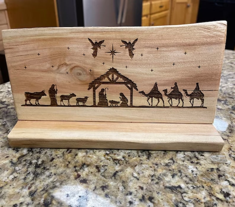 May include: A wooden Christmas nativity scene with a brown wood base. The scene features a manger with the baby Jesus, Mary, and Joseph. There are also angels, a star, and three wise men riding camels.