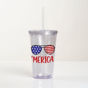 May include: Clear plastic tumbler with a straw, featuring a red, white, and blue American flag design with sunglasses and the text 'MERICA'.