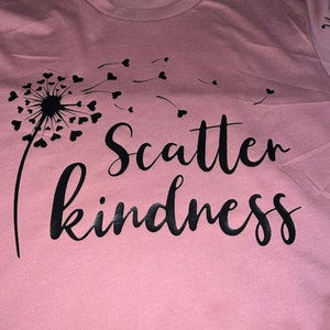 May include: A pink t-shirt with a black dandelion design and the text "Scatter kindness" printed on it.