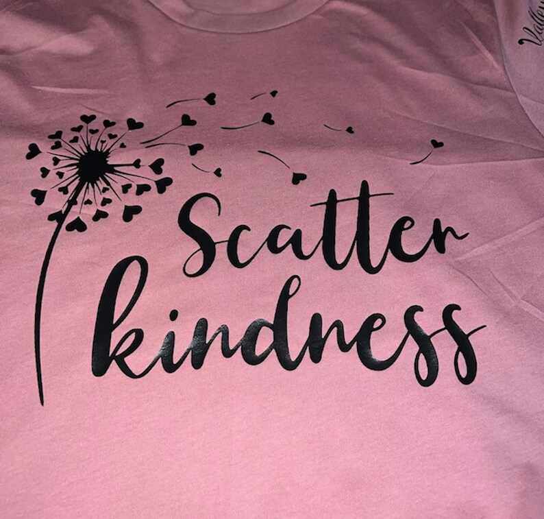 May include: A pink t-shirt with a black dandelion design and the text "Scatter kindness" printed on it.