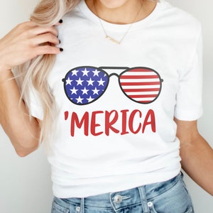 May include: White t-shirt with a graphic of sunglasses with an American flag design and the text 'MERICA' in red.