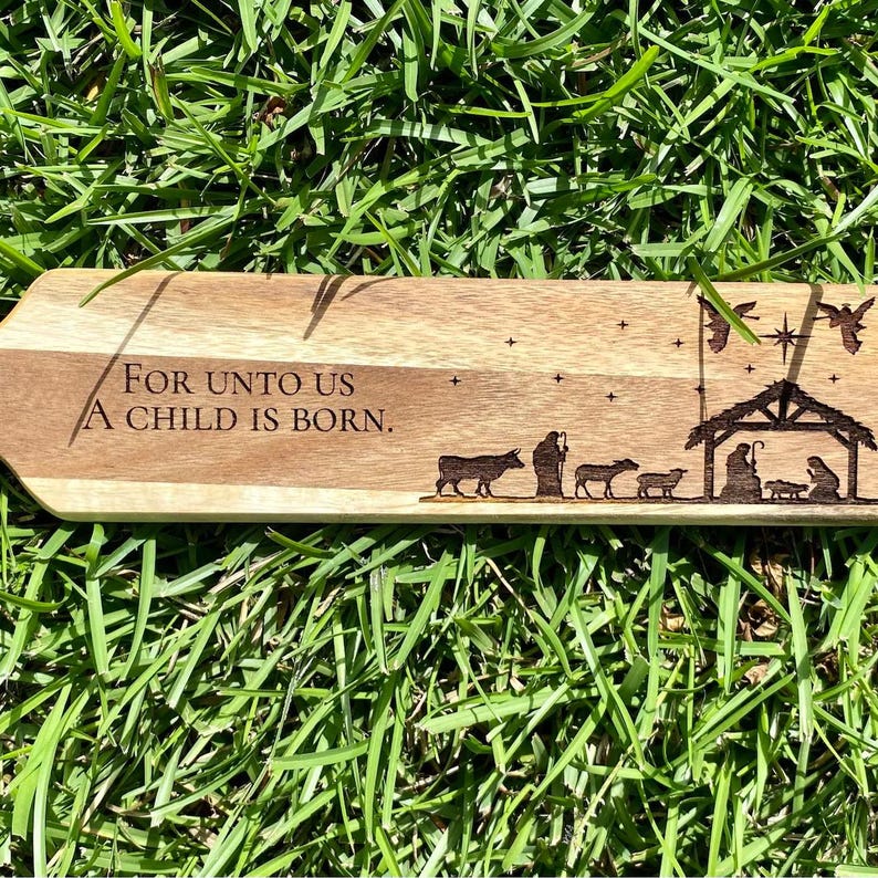 May include: A wooden Christmas ornament with the text "For unto us a child is born." and a silhouette of the nativity scene.