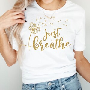 May include: White t-shirt with a gold glitter design of a dandelion with the words "just breathe" underneath.