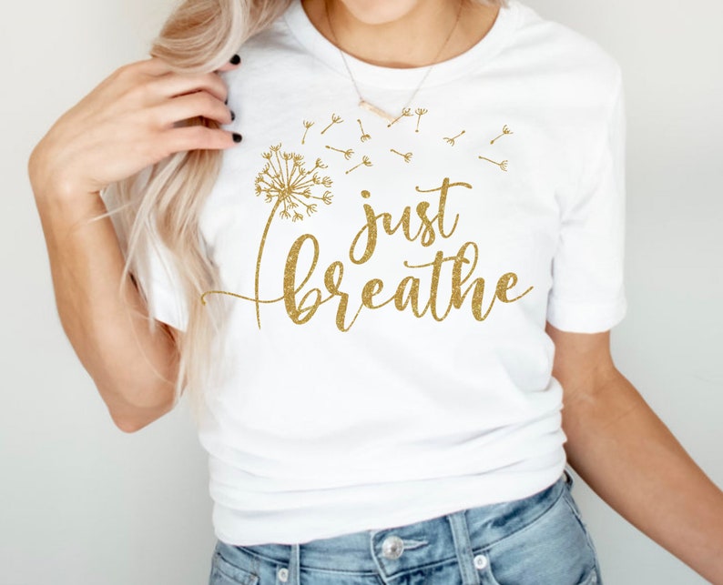 May include: White t-shirt with a gold glitter design of a dandelion with the words "just breathe" underneath.