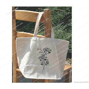 May include: A white tote bag with a black floral design. The bag is sitting on a wooden chair.