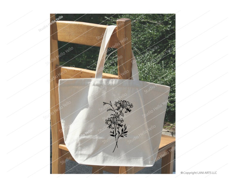May include: A white tote bag with a black floral design. The bag is sitting on a wooden chair.