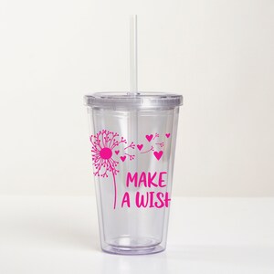 May include: Clear plastic tumbler with a pink dandelion design and the text "Make a Wish". The tumbler has a lid and a straw.