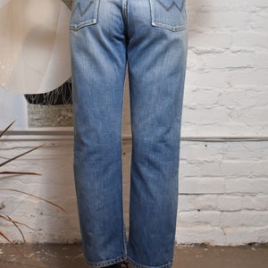 K&ouml;nnte beinhalten: Eine hellblaue Jeans mit einem braunen Leder-Patch auf der Ges&auml;&szlig;tasche. Die Jeans hat einen geraden Schnitt und eine lockere Passform.
