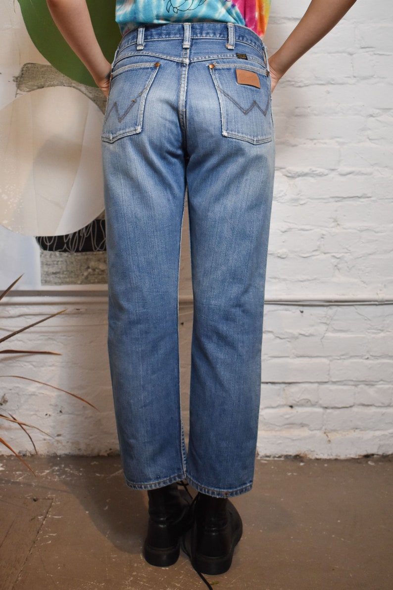 K&ouml;nnte beinhalten: Eine hellblaue Jeans mit einem braunen Leder-Patch auf der Ges&auml;&szlig;tasche. Die Jeans hat einen geraden Schnitt und eine lockere Passform.