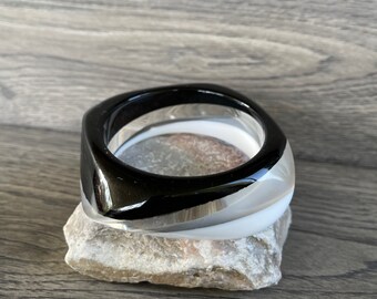 May include: Two black and white plastic bangles stacked on top of each other. The top bangle is black with a white stripe, and the bottom bangle is white with a black stripe.