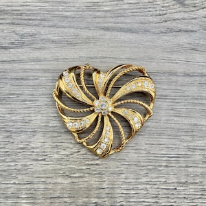 May include: A gold-tone heart-shaped brooch with a swirling design and clear rhinestones.