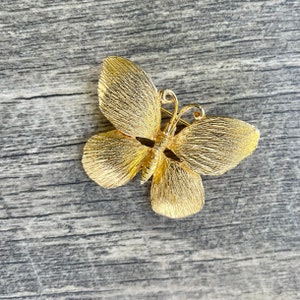 May include: A gold-toned butterfly brooch with a textured finish. The brooch is a delicate and intricate design.