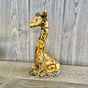 May include: A ceramic giraffe figurine with a brown, black, and white patterned design. The giraffe is standing on a wooden surface.