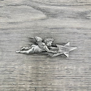 May include: A silver cherub angel figurine flying with a star. The angel is holding the star with one hand and has wings spread out. The star has a textured surface.