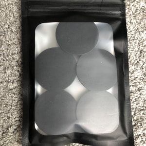 Puede incluir: Una bolsa de plástico transparente con cierre de cremallera negra contiene seis agarres redondos de teléfono negros.