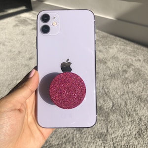 May include: A white iPhone with a pink glitter phone grip.