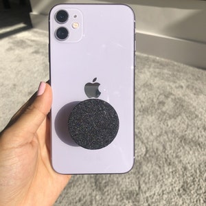 May include: A lavender iPhone with a black glitter phone grip.