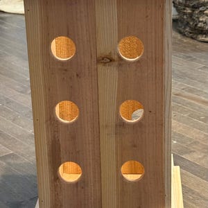 May include: A tall, rectangular wooden structure with a square top and base. The sides have evenly spaced circular cutouts. The natural wood is light brown, and the construction appears sturdy.