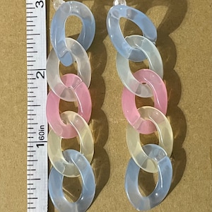 May include: A pair of long, pastel-colored chain earrings. The earrings are made of plastic and have a light blue, white, and pink color scheme.