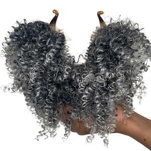 Peut inclure: Deux extensions de cheveux bouclés gris et argent avec des clips bruns. Les extensions sont tenues dans une main.