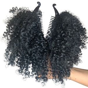 Puede incluir: Dos extensiones de pelo rizado negro con clips. Las extensiones están sujetas por una mano.