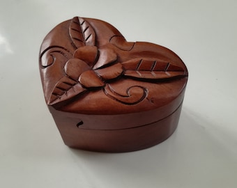 May include: A heart-shaped wooden box with a carved floral design. The box is made of dark brown wood and has a hinged lid.