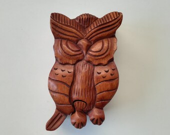 Op de afbeelding: Een gesneden houten uil beeldje in bruine tinten. De uil heeft gedetailleerde veersculpturen, grote ogen en een prominente snavel. Het beeldje is een decoratief item, waarschijnlijk voor de interieurdecoratie.