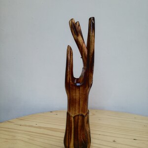 K&ouml;nnte beinhalten: Eine Holzskulptur einer Hand mit nach oben ausgestreckten Fingern. Die Skulptur besteht aus dunkelbraunem Holz mit gl&auml;nzender Oberfl&auml;che. Die Hand ist mit detaillierten Linien und Texturen geschnitzt, vor hellem Hintergrund.