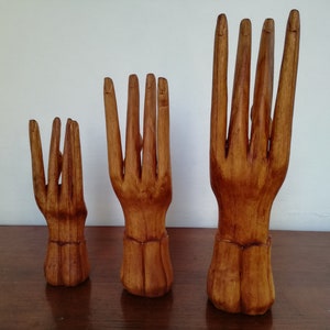 Puede incluir: Tres soportes de anillos de madera con forma de mano en diferentes tama&ntilde;os. Las manos est&aacute;n talladas con detalles realistas y tienen un acabado de madera natural.
