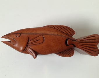 May include: A wooden fish-shaped puzzle box with a detailed carving of the fish's scales and fins. The box is made of a rich brown wood.
