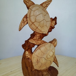 May include: Hand-carved wooden sculpture of two sea turtles, one on top of the other, with intricate details. The turtles are brown and have a natural wood finish.