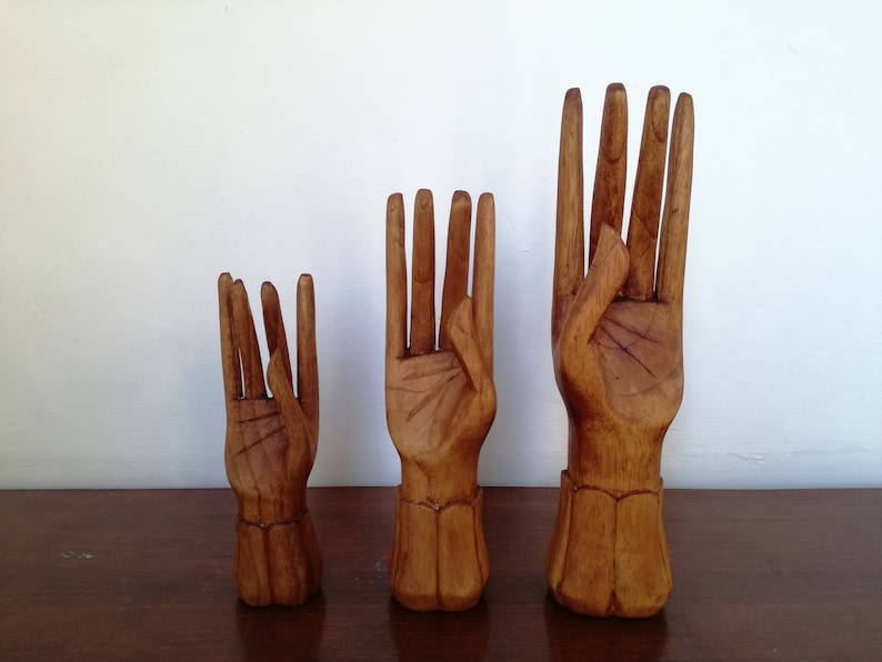 Puede incluir: Tres esculturas de manos de madera en diferentes tama&ntilde;os. Las manos est&aacute;n talladas en madera natural y tienen un acabado liso. Las manos est&aacute;n dispuestas en fila de la m&aacute;s peque&ntilde;a a la m&aacute;s grande.