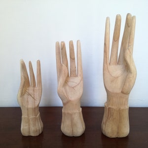 Puede incluir: Tres esculturas de manos de madera en diferentes tama&ntilde;os. Las manos est&aacute;n talladas en un estilo realista y tienen un acabado de madera natural.