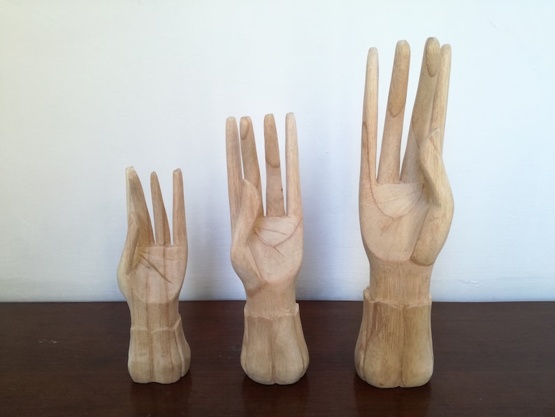 Puede incluir: Tres esculturas de manos de madera en diferentes tama&ntilde;os. Las manos est&aacute;n talladas en un estilo realista y tienen un acabado de madera natural.