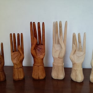 Puede incluir: Seis esculturas de manos de madera en varios tama&ntilde;os y tonos de marr&oacute;n. Las manos est&aacute;n talladas en un gesto de ofrecimiento o entrega.