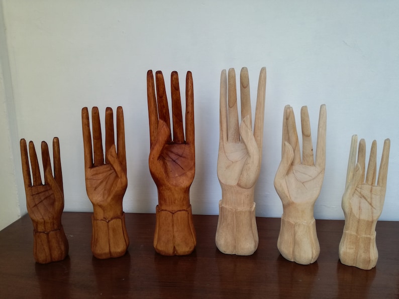 Puede incluir: Seis esculturas de manos de madera en varios tama&ntilde;os y tonos de marr&oacute;n. Las manos est&aacute;n talladas en un gesto de ofrecimiento o entrega.