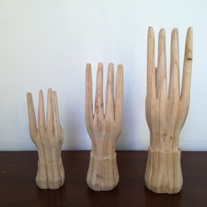 Puede incluir: Tres expositores de madera con forma de mano en diferentes tama&ntilde;os. Las manos est&aacute;n todas en una pose similar con los dedos extendidos y ligeramente separados.