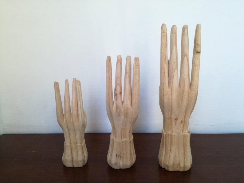 Puede incluir: Tres expositores de madera con forma de mano en diferentes tama&ntilde;os. Las manos est&aacute;n todas en una pose similar con los dedos extendidos y ligeramente separados.