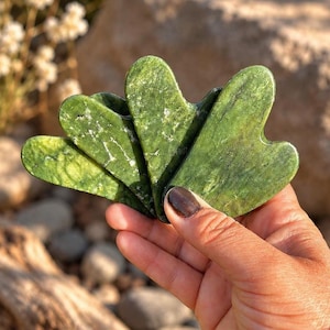 May include: A set of three heart-shaped gua sha tools crafted from mottled dark green stone with visible white veining. Each tool features a smooth, polished surface with multiple curved edges and indentations designed for facial massage applications.