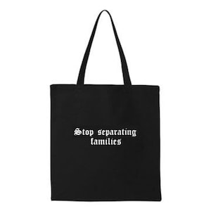 May include: Black tote bag with long handles. The bag features the white text "Stop separating families" in a gothic font. The bag is made of a sturdy material and is designed for carrying items.