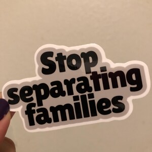 May include: A gray and white sticker with the text "Stop separating families" in black.