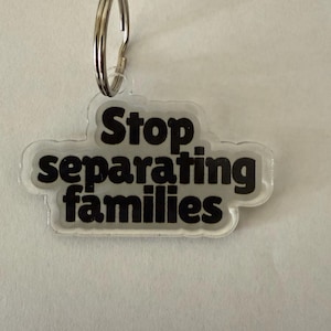 May include: A clear acrylic keychain with the phrase "Stop separating families" in black, bold lettering. The keychain has a silver metal ring for attaching to keys or bags. The text is in a rounded font.
