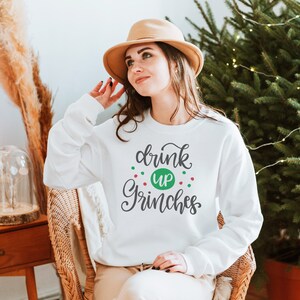 May include: White sweatshirt with the text "drink up Grinches" in gray script with green and red dots around the text.
